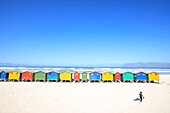 Südafrika, Westkap, Surfer in der Nähe von bunten Strandhütten am Muizenberg Beach in Kapstadt