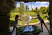 France, Lot et Garonne, Le Temple-sur-Lot, Latour-Marliac water lily garden, children playing under the waterfall in the cave of the landscaped park