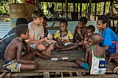 Papua New Guinea, East Sepik Province, Sepik River Region, Angoram District, Samban Village, one of the two sons of US Missionary Jesse Pryor playing cards with local kids