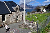 United Kingdom, Scotland, Highlands, Hebrides, Isle of Skye, Elgol village on the shores of Loch Scavaig towards the end of the Strathaird peninsula and the Black Cuillin Mountains in the background, children playing rounders in the school garden