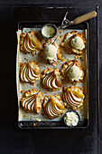 Freshly baked pear and almond tartlets, on brown baking paper, finished with vanilla ice cream on a black baking tray