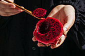 Dragon fruit,also called pitaya,sliced pink magenta-coloured flesh with tiny black seeds,in the hands of a woman,tropical fruit