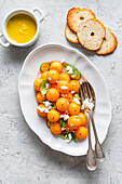 Melonenkugeln mit Rucola,Feta und Gurkenscheiben,garniert mit Basilikumblättern und Pfeffer. Kleine Schale mit Sauce aus Melone und Gurke,Salz und Öl. Ansicht von oben. Platz zum Kopieren.