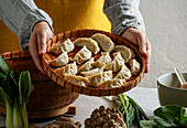 Female chef holding a bamboo tray with uncooked gyoza dumplings,bamboo steamer,teapot,fresh green onions and mushrooms,Asian cuisine