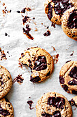 An assortment of chocolate chip cookies with a bite taken out of one, resting on parchment paper, showcasing melted chocolate and a sprinkle of sea salt.