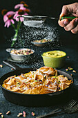 Side shot of a cast iron pan with curled phyllo, action with male hand holding a sieve with icing sugar