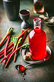 Beautiful glass bottle with purple rhubarb syrup and syrup in a spoon,with fresh rhubarb stalks and cocktail jigger in the background
