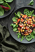 Salat mit Kichererbsen,schwarzem Reis,Tomaten,Mandeln und Grünzeug auf einem schwarzen Teller. Schwarzer Hintergrund