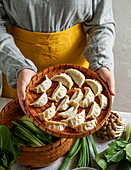 Cook holding a bamboo tray with uncooked gyoza dumplings,bamboo steamer,teapot,fresh green onions and mushrooms,Asian cuisine