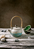 Original handmade ceramic teapot with wooden handle and cups for traditional Chinese tea drinking on an old wooden table. Decorative sea pebbles all around. Copy space