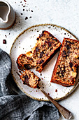 A delicious slice of chocolate chip banana bread served on a speckled plate with a fork and a gray linen napkin nearby.