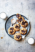 A plate of freshly baked chocolate chip cookies with a side of milk and sea salt on a textured surface.