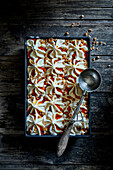 Homemade caramel ice cream,with caramel sauce,caramelised walnut pieces,in a baking dish on a dark wooden base with an old ice cream scoop