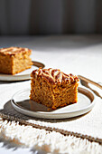 Square of pumpkin pie with swirls of almond butter on neutral background with golden forks