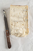 A slice of Italian cheese called Gorgonzola lying on the paper it was wrapped in. Front view