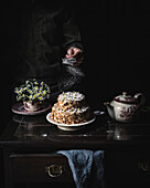 Atmospheric scene with an almond cake as the main dessert. Background with flowers, a teapot and a blue linen cloth on an old table