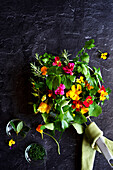 Cooking with herbs and edible flowers concept. Frypan skillet on dark background.