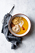 An assortment of ingredients for a recipe is displayed in a bowl, including mashed bananas, tahini, oil, and spices, with a whisk and a gray cloth nearby.