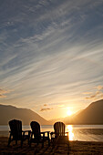 Three Adirondack style wooden lounge chairs at Crescent Lake Lodge at Olympic National Park at sunset.