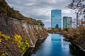 View along the inner Osaka Castle moat with autumnal trees and Crystal tower and CBD in the background, Osaka, Honshu, Japan, Asia