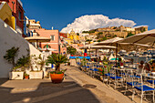 View of restaurants in Marina di Corricella and Church of Santa Maria delle Grazie in background, Procida, Phlegraean Islands, Gulf of Naples, Campania, Southern Italy, Italy, Europe