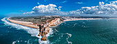 A breathtaking aerial drone panoramic view of Nazare's coastline with towering cliffs meeting the ocean, and waves crashing onto the sandy beach, Nazare, Oeste, Estremadura, Portugal, Europe