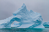 Ungewöhnliche Fensterformation in einem Eisberg mit Booth Island im Hintergrund auf der westlichen Seite der Antarktischen Halbinsel,Antarktis,Polargebiete