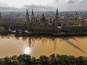 Aerial view of an abundant passing by El Pilar Basilica Cathedral after the Dana, Zaragoza, Spain