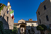 Ein traditionelles Gebäude mit italienischer Flagge in der Borga oder mittelalterlichen Hügelstadt Farfa,Italien. In der Mitte befindet sich das Tor zur Abtei von Farfa.