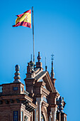 Close up of the intricate architectural details of Plaza de España in Seville, Spain, featuring traditional Spanish design elements and a vibrant flag against a clear blue sky.