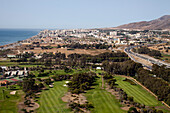 An aerial perspective showcases the beautiful coastline and urban areas of Malaga, highlighting its green spaces and coastal roads.