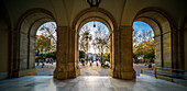 Seville, Spain, Jan 28 2021, A picturesque view from under the arched portico of Seville's Town Hall, revealing the vibrant plaza with pedestrians, trees, and architecture in the background under a clear blue sky.