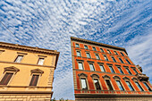 Klassische römische Gebäude mit lebhaften Fassaden unter einem dramatischen wolkengefüllten Himmel.