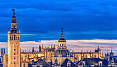 A breathtaking aerial view showcasing Seville's Giralda Tower, majestic Cathedral, and El Salvador Church dome under a vivid blue sky, highlighting the city's rich historical architecture.