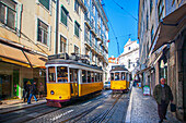 Lisbon, Portugal, March 1 2007, Two trams travel along Rua da Conceicao, capturing the vibrant urban life of Baixa, Lisbon, with buildings and clear blue skies.