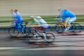 Panning shot capturing the dynamic movement of cyclists racing through the city streets at night, creating a vibrant blur of colors and motion.