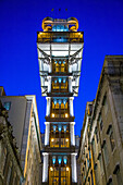 The Santa Justa Elevator in Lisbon's Baixa district glows with vibrant lights against the night sky, showcasing its architectural beauty and historical significance.