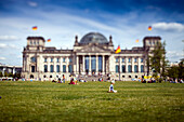 Visitors relax on the green lawn near the historic Reichstag building in Berlin, enjoying a sunny day in the heart of the city.