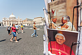 Rome, Italy, July 22 2017, Postcards depicting popes Benedict XVI and John Paul II are displayed in Vatican City, with tourists strolling nearby under the sun.