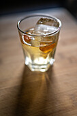 A close up of a refreshing whiskey cocktail garnished with orange peel and ice, captured in the vibrant city of Seville, Spain. Perfect for leisure and celebration settings.