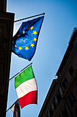 The vibrant flags of Italy and the European Union fly high against a clear blue sky in Rome, capturing the essence of the city.