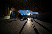 A striking image of silhouetted figures walking beneath Las Setas in Seville, Spain, during sunset. The dramatic architecture and long shadows create a captivating urban scene.