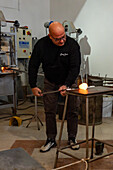 The glassblower rolls the molten gather on a marver in a glassblowing demonstration in Venice, Italy. Marvering creates a skin on the surface of the glass an begins to shape the gather.