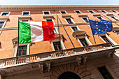 Italian and EU flags display on historic Rome building facade.