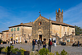 Tourists in front of the Church of Santa Maria Assunta in the walled medieval town of Monteriggioni, Italy. The church faces the Piazza Roma.