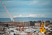 Stunning aerial view of Seville showcasing the illuminated bell tower of Omnium Sanctorum church with the modern Alamillo Bridge in the background, highlighting the city's architectural contrast.