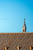 Ein klarer blauer Himmel über einem traditionellen Dach in Sevilla,Spanien,mit dem ikonischen Turm La Giralda im Hintergrund,der den historischen Charme der Stadt einfängt.