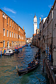 Two gondolas carrying tourists in a canal in Venice, Italy. Behind is the leaning bell tower or campanile of the Greek Orthodox Church of San Giorgio dei Greci.