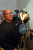 The heat of the glass ignites a piece of paper in flames in a glassblowing demonstration in Venice, Italy. The glassblower is showing how hot the glass still is.