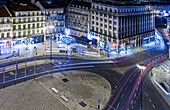 The vibrant nightlife of Restauradores Square in Lisbon showcases light trails from cars navigating the urban streets at night.